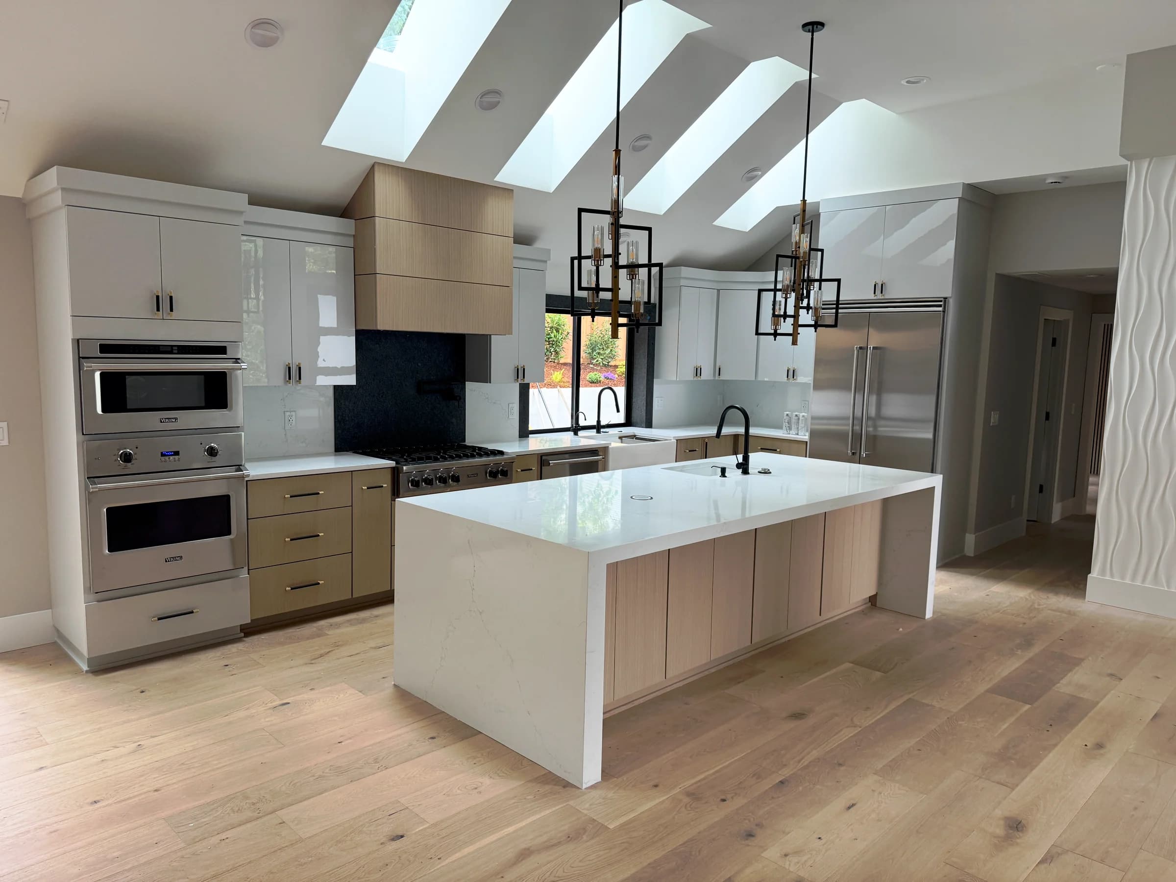 NS Wood Finishing project: a sunlit kitchen with light wood base cabinets, white upper cabinets and a waterfall island