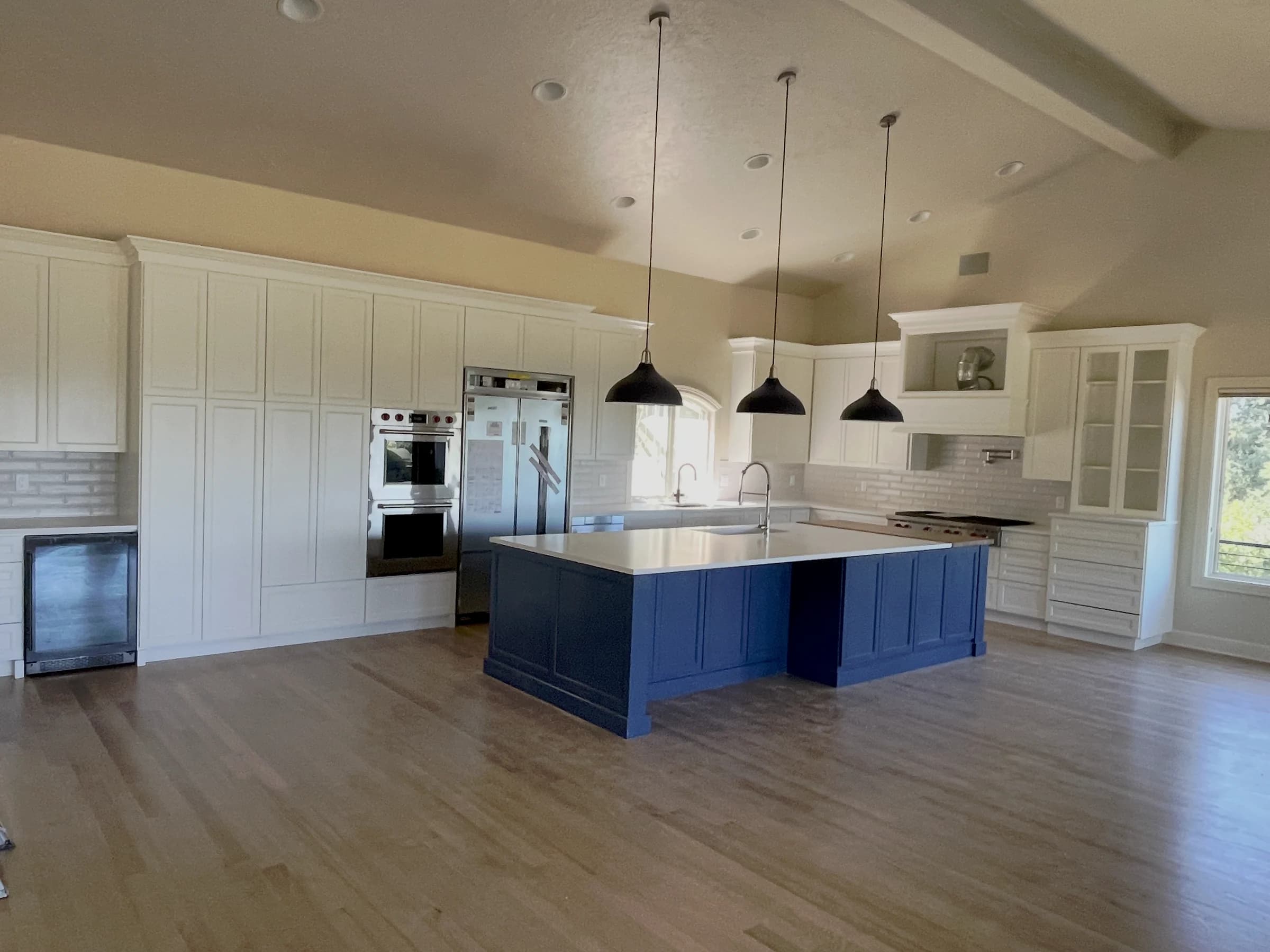 NS Wood Finishing project: white kitchen cabinets around a dark blue island with black pendant lights